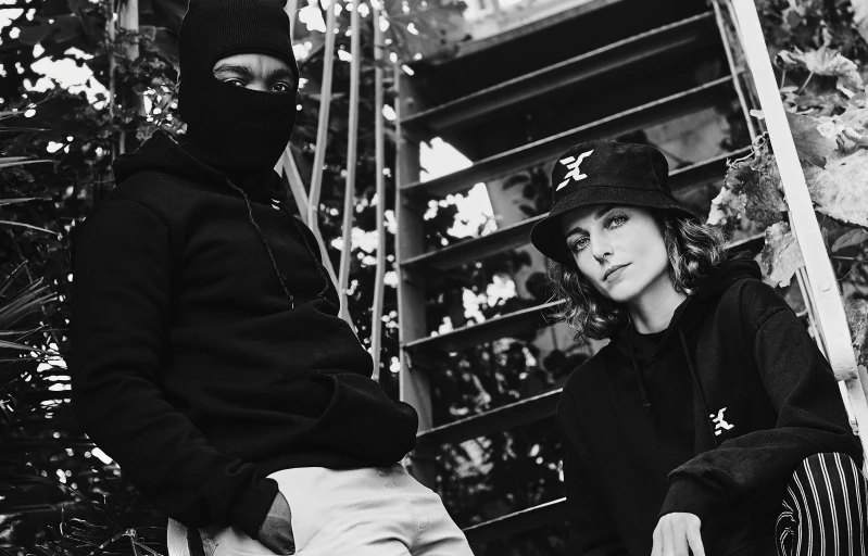 a couple of people standing next to each other, a black and white photo, antipodeans, ninja outfit, woman in streetwear, black hat, black man