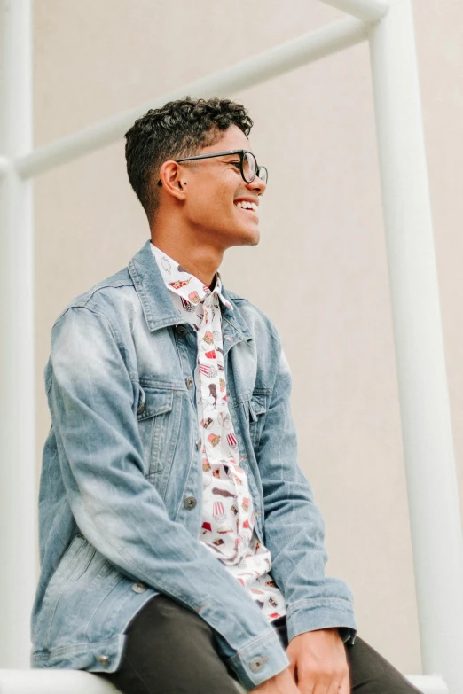 a man sitting on a ledge wearing a shirt and tie, trending on pexels, jean jacket, cute slightly nerdy smile, non binary model, patterned clothing