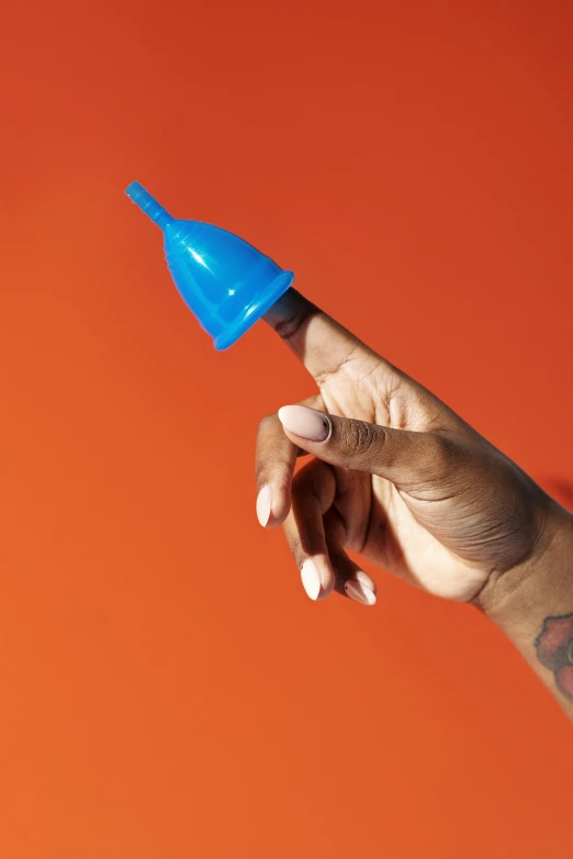 a person holding a blue object in their hand, piercing, in front of an orange background, cone shaped, blue undergarments