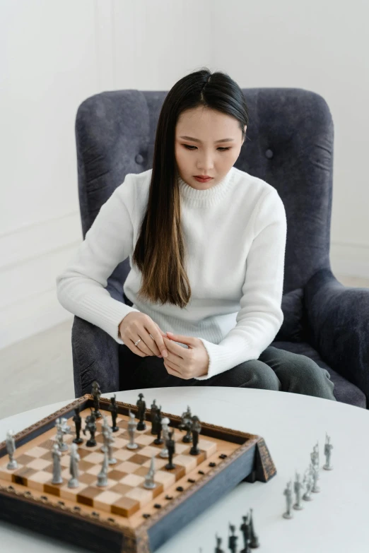 a woman sitting in a chair playing a game of chess, inspired by Fei Danxu, pexels contest winner, on a white table, wearing a turtleneck and jacket, battle ready, katherine lam