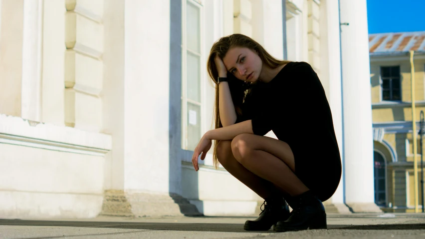 a woman sitting on the ground in front of a building, pexels, realism, sad frown, black, anorexic figure, concerned