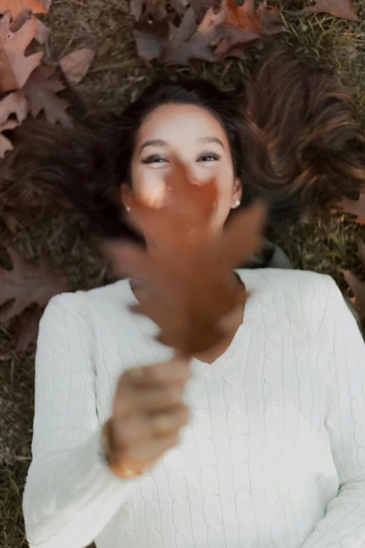 a woman laying on the ground surrounded by leaves, a picture, trending on unsplash, wave a hand at the camera, video still, with brown hair, smiling down from above