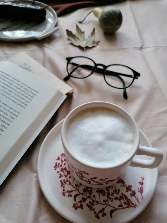 a cup of coffee and a book on a table, by Lucia Peka, wearing black frame glasses, cappuccino, close-up photo, multiple stories