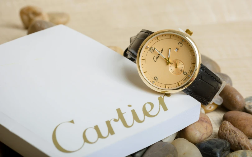 a watch sitting on top of a box next to rocks, inspired by Cafer Bater, pexels contest winner, cartier, beige, thumbnail, circular