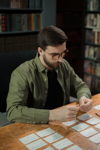 a man sitting at a table with papers in front of him, inspired by Christoffer Wilhelm Eckersberg, pexels contest winner, trading card game, library nerd glasses, lgbtq, high quality screenshot