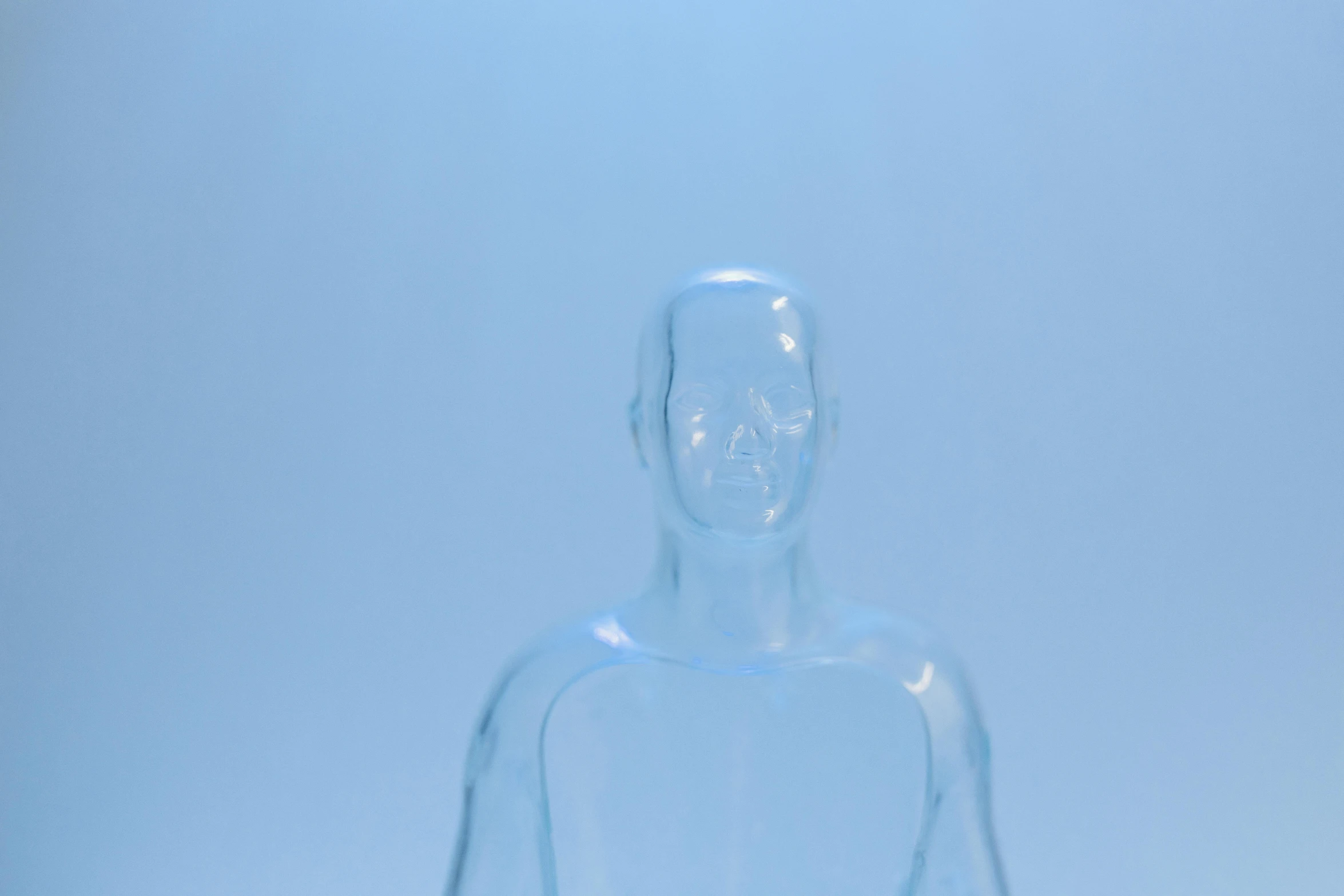a clear figurine sitting on top of a table, plasticien, freezing blue skin, looking straight into camera, general human form, medical image