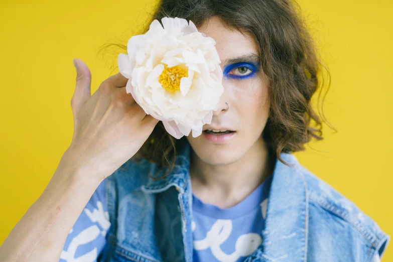 a woman holding a flower in front of her face, an album cover, trending on pexels, attractive androgynous humanoid, blue eyeball, paul atreides, in blue and yellow clothes