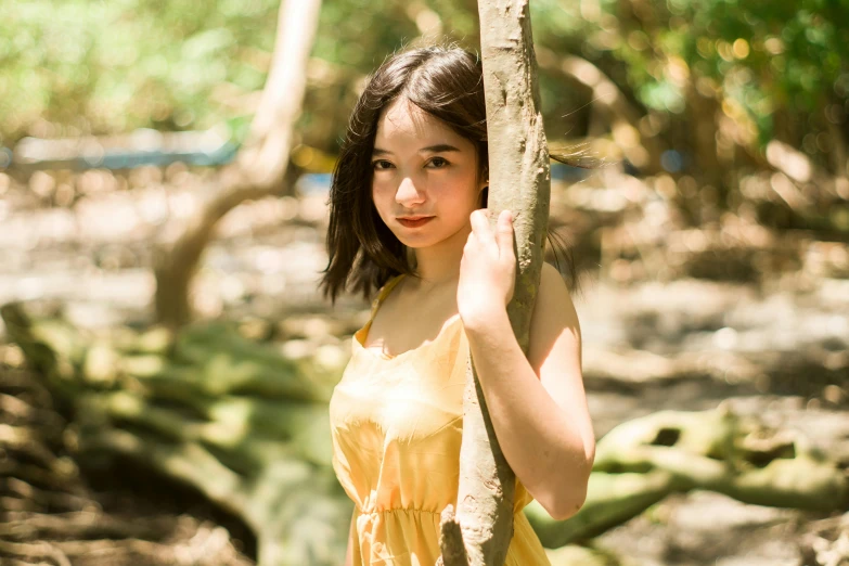 a woman in a yellow dress standing next to a tree, inspired by Kim Du-ryang, unsplash, young cute wan asian face, wearing a camisole and shorts, gemma chan, portrait image
