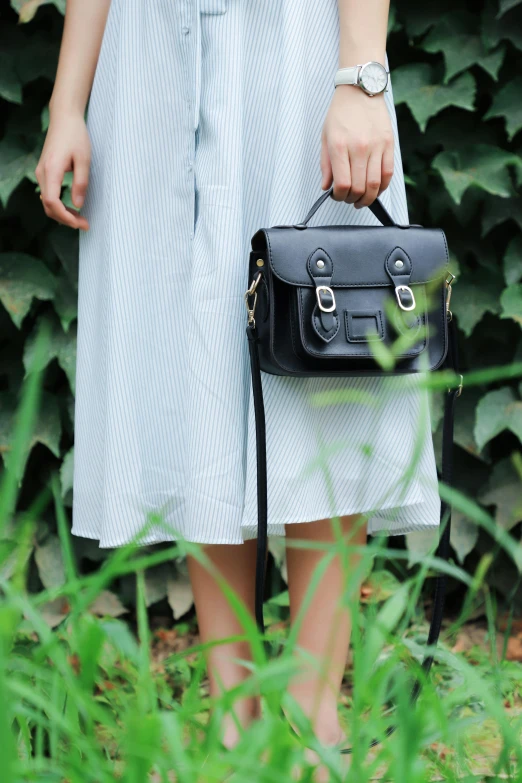 a woman in a white dress holding a black bag, by Julia Pishtar, unsplash, square backpack, greenery, retro stylised, english style