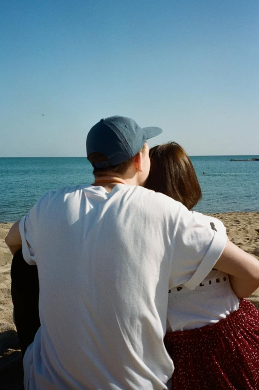 a man and a woman are sitting on the beach, a picture, by Nina Hamnett, unsplash, agrigento, arm around her neck, taken in the late 2000s, with his back turned