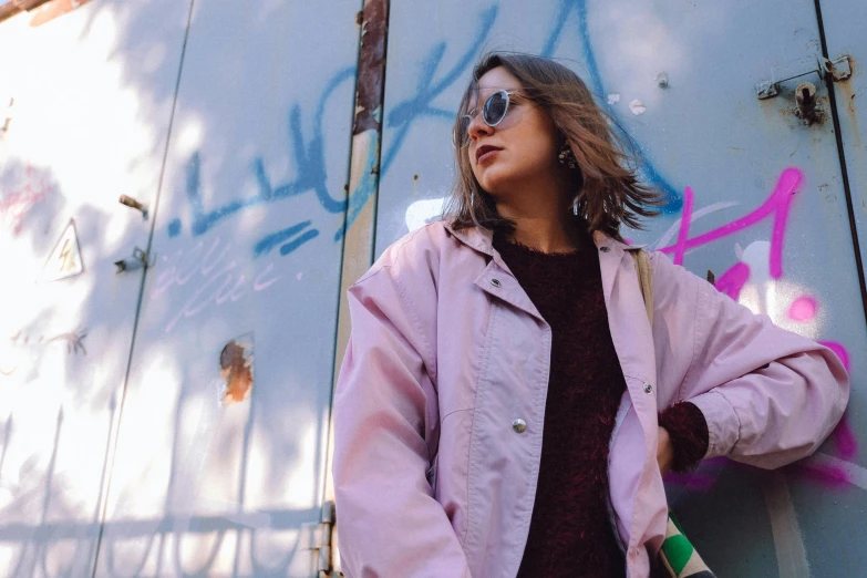 a woman standing in front of a wall with graffiti on it, trending on pexels, pink pastel, wearing an aviator jacket, instagram photo, lo fi