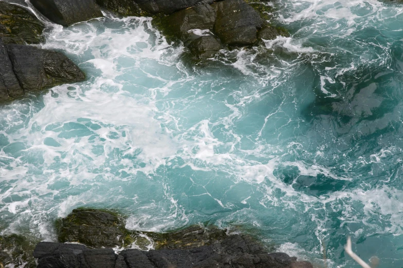 a person riding a surfboard on top of a body of water, rocky cliff, turquoise palette, whirlpool, cornwall