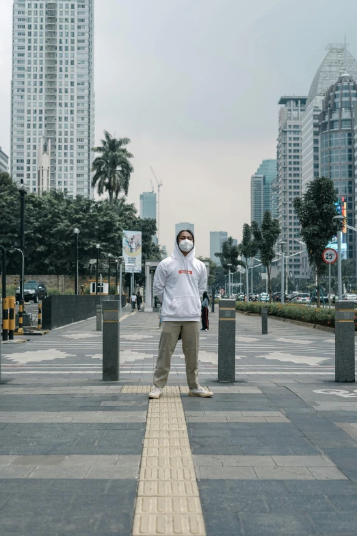 a man wearing a face mask standing in the middle of a street, inspired by Cheng Jiasui, pexels contest winner, jakarta, wearing a hoody, avatar image, high rises