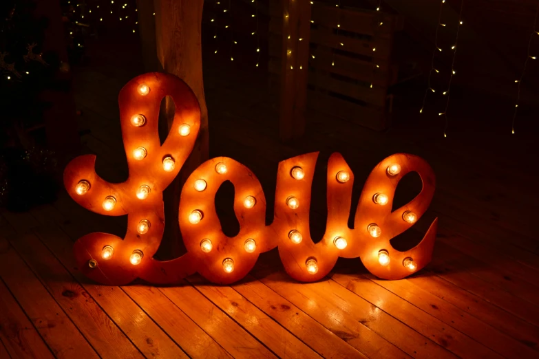 a lighted love sign sitting on top of a wooden floor, a picture, copper, reddish exterior lighting, detailed shot, cosy