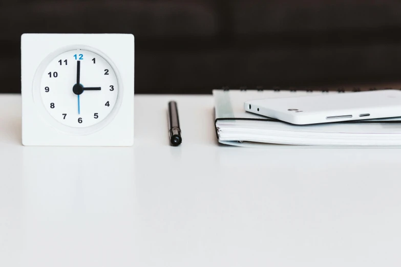 a white clock sitting on top of a white table, unsplash, sitting at a desk, rectangle, a close-up, uploaded