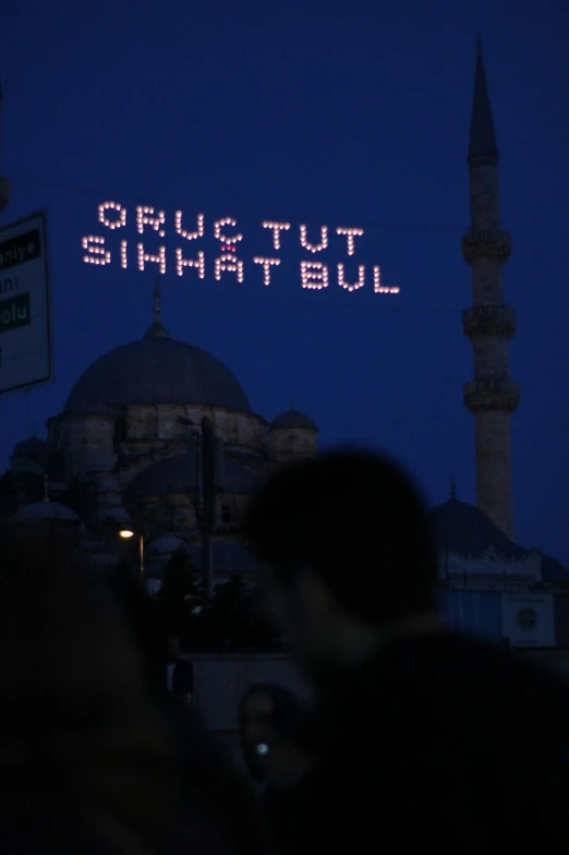 people standing in front of a building with a message on it, by Muggur, hurufiyya, emitting light ornaments, streetlights, dug stanat, ap news photograph