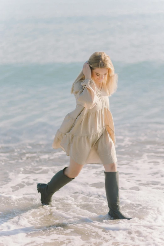 a woman walking on a beach next to the ocean, inspired by Oleg Oprisco, unsplash, knee-high boots, dressed anya taylor - joy, beige, smol