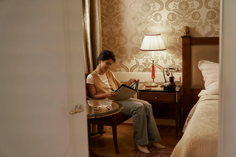 a woman sitting in a chair reading a book, by Konrad Witz, pexels contest winner, rococo, hotel room, wes anderson and gucci, maggie cheung, serene bedroom setting