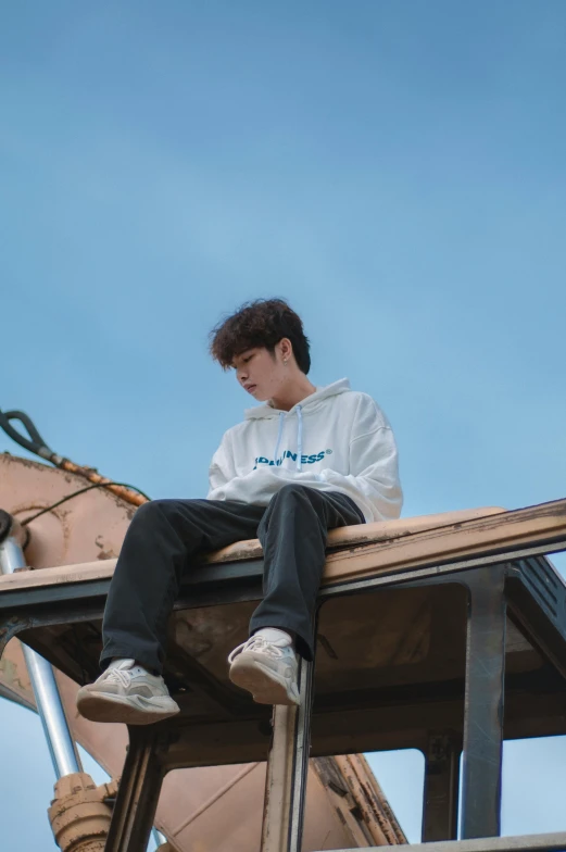 a man sitting on top of a wooden structure, an album cover, inspired by jeonseok lee, trending on pexels, realism, blue hoodie, uniform off - white sky, 15081959 21121991 01012000 4k, l · lawliet