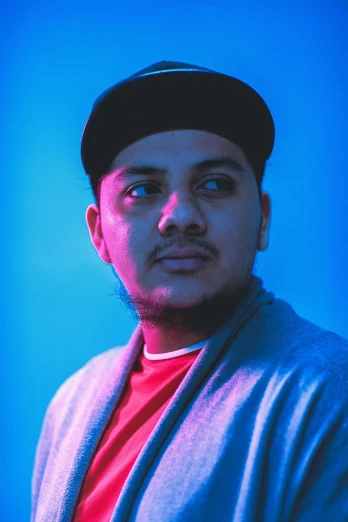 a man standing in front of a blue background, an album cover, inspired by Eddie Mendoza, unsplash, hurufiyya, red and blue back light, headshot profile picture, sitting down casually, indian