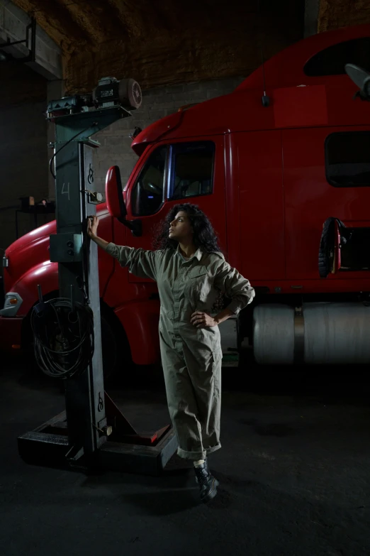 a man standing next to a large red truck, a portrait, by Jim Murray, pexels contest winner, woman in a dark factory, mechanic, photo of a black woman, woman and robot