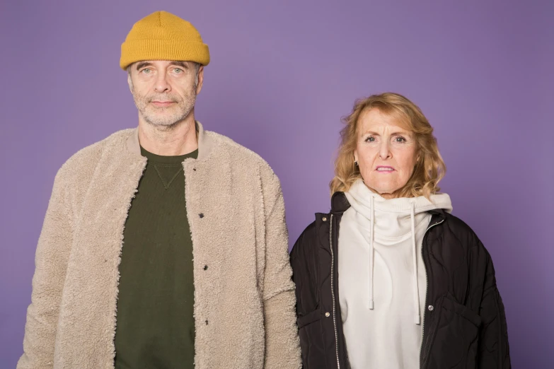 a man and a woman standing next to each other, wearing a purple cap, grumpy [ old ], matt mute colour background, joel fletcher