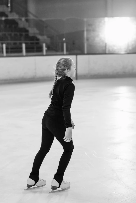 a woman riding a skateboard on top of an ice rink, a black and white photo, by Maggie Hamilton, unsplash, arabesque, wearing a black catsuit, looking from behind, a blond, indoor picture