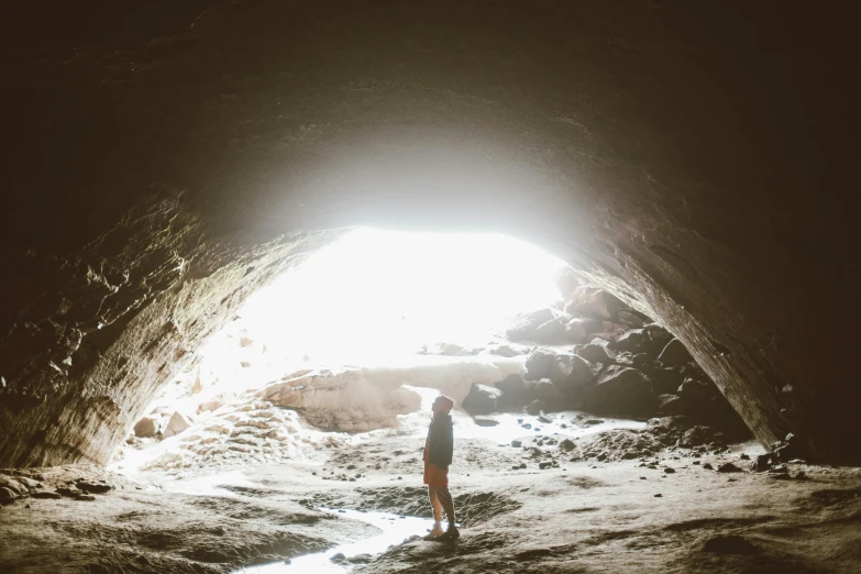 a person standing in front of a light at the end of a cave, by Jessie Algie, unsplash contest winner, kauai, summer light, instagram post, cave town