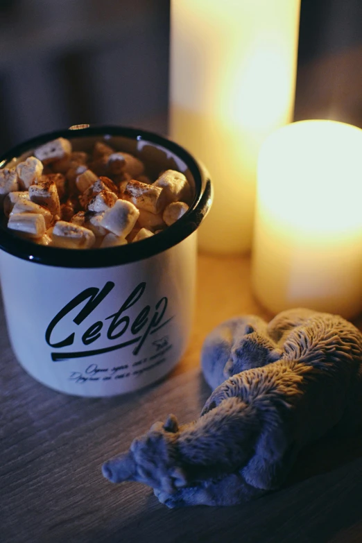 a cup of hot chocolate with marshmallows next to a candle, inspired by Elsa Bleda, les nabis, cereal, cosy vibes, profile image