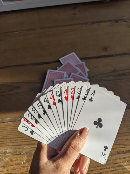 a person holding playing cards on a wooden table, by Tom Wänerstrand, pexels contest winner, hyperrealism, taken on iphone 14 pro, light pink tonalities, multiplayer set-piece, instagram story