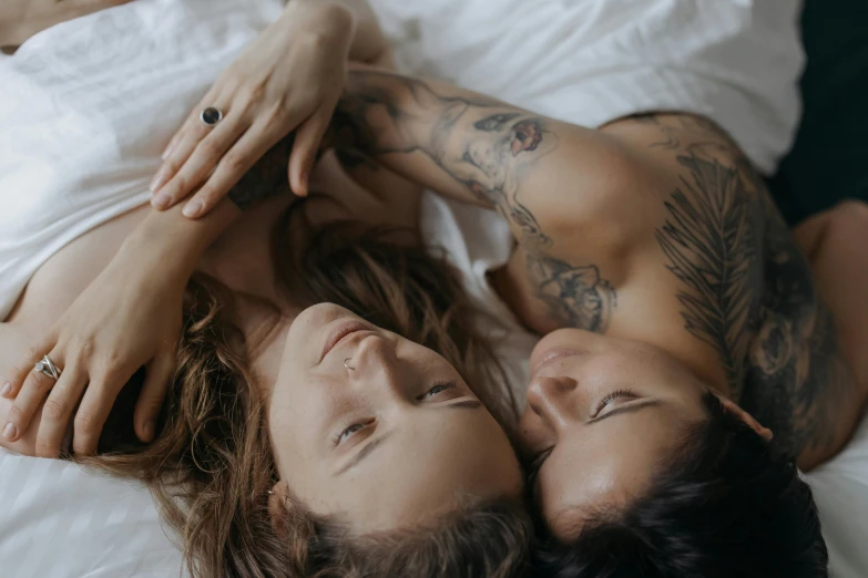 a man and a woman laying on top of a bed, a tattoo, trending on pexels, lesbian embrace, beautiful gemini twins portrait, gif, one blonde and one brunette