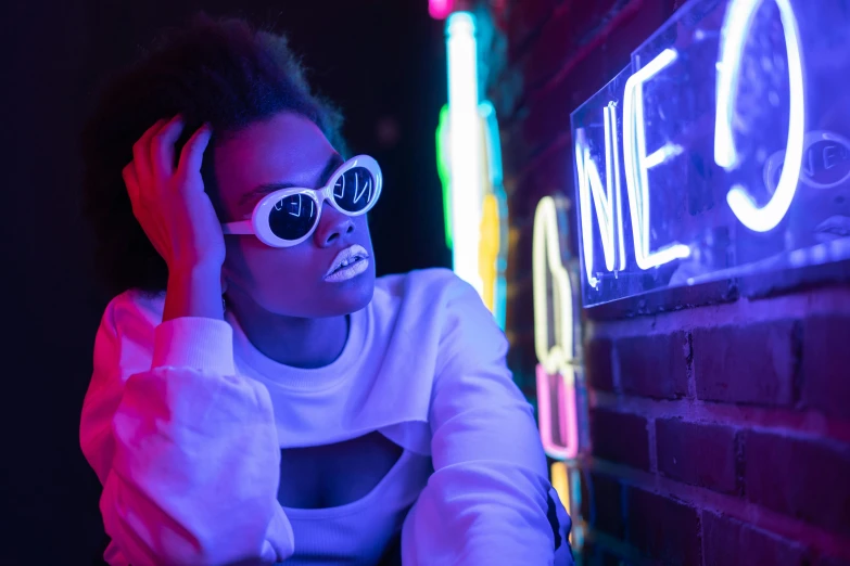 a woman sitting in front of a neon sign, trending on pexels, afrofuturism, digital sunglasses, white neon, mid night, ( ( dark skin ) )