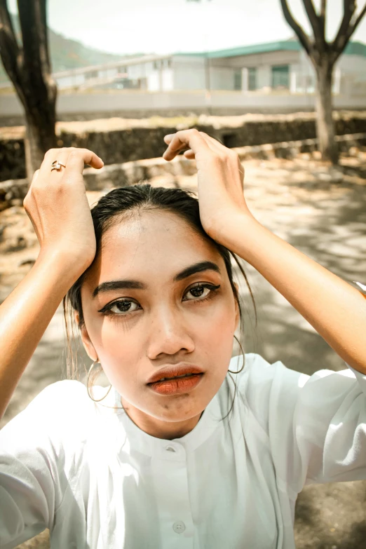 a woman standing under a tree with her hands on her head, by Basuki Abdullah, trending on pexels, realism, big eyebrows, frown fashion model, selfie of a young woman, clean symmetrical face