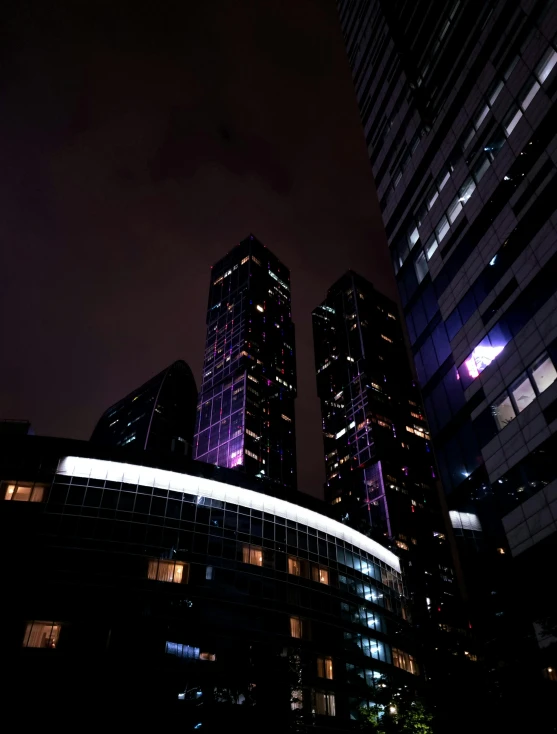 a group of tall buildings lit up at night, an album cover, pexels contest winner, cool purple grey lighting, neo kyiv, low quality photo, taken in the late 2010s