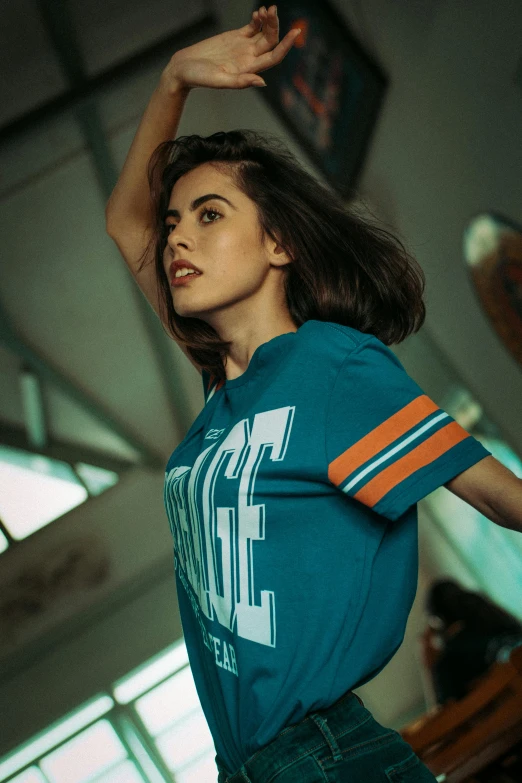 a woman in a blue shirt is dancing, a colorized photo, inspired by Elsa Bleda, pexels contest winner, wearing basketball jersey, teal orange, young beautiful amouranth, streetwear fashion
