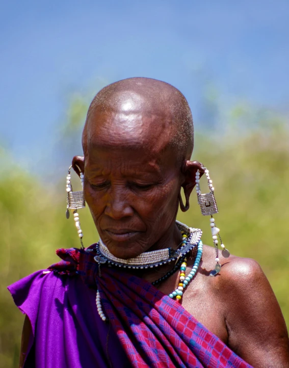 a close up of a person wearing a purple dress, by Hannah Tompkins, trending on unsplash, afrofuturism, massai warrior, an oldman, queer woman, standing in the savannah