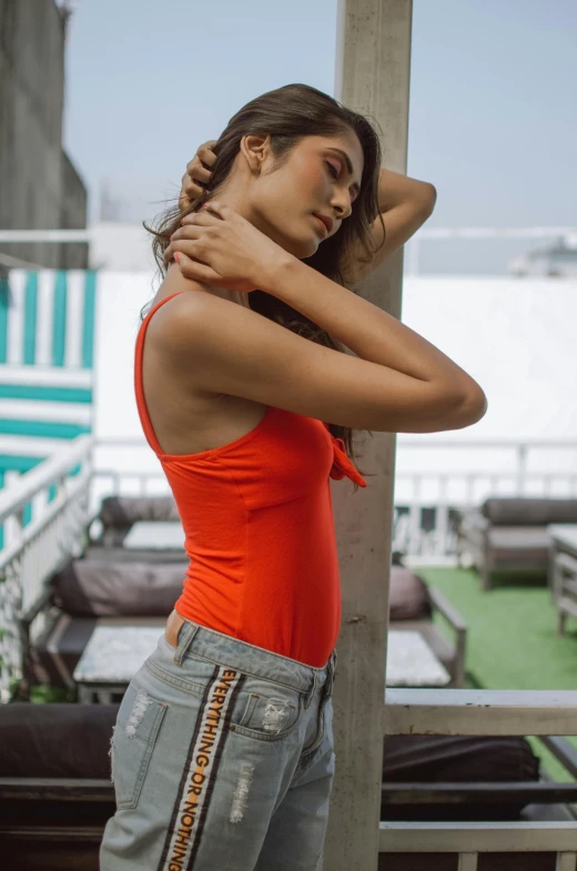 a woman in an orange tank top leaning against a pole, trending on pexels, bodysuit, at the terrace, indian super model, denim