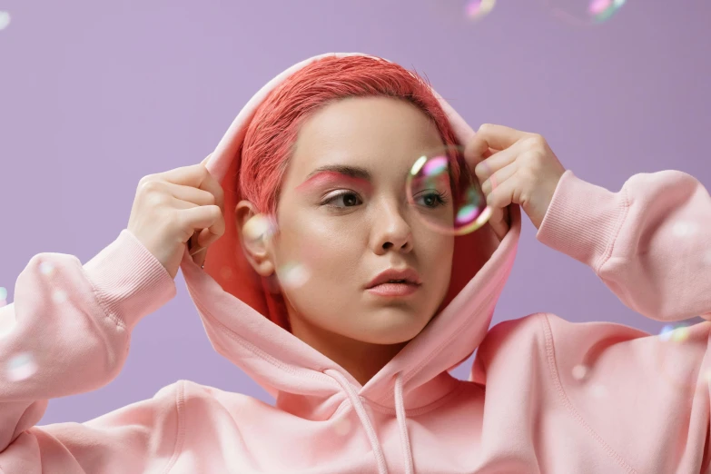 a woman in a pink hoodie blowing bubbles, inspired by Pearl Frush, trending on pexels, magic realism, pink short hair, bella poarch, skincare, complementary colour