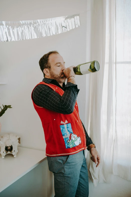 a man in a red vest drinking from a bottle, inspired by Don Eddy, pexels contest winner, wearing festive clothing, dan harmon, wearing jacket, at home