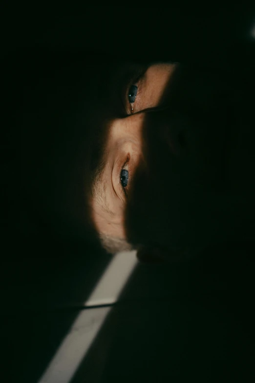a close up of a person in a dark room, a picture, looking down at you, slight lens glare, shadow filled room with gloomy, looking down on the camera