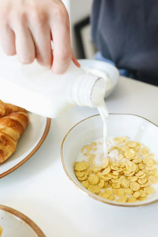 a person pouring milk into a bowl of cereal, white with gold accents, toast, uncrop, french