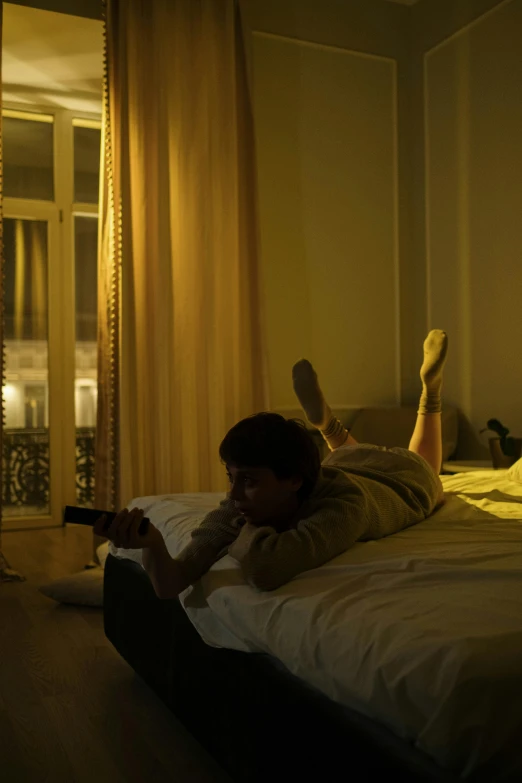 a man laying on top of a bed next to a window, inspired by Nan Goldin, unsplash contest winner, checking her phone, watching tv, perfectly lit. movie still, paris hotel style