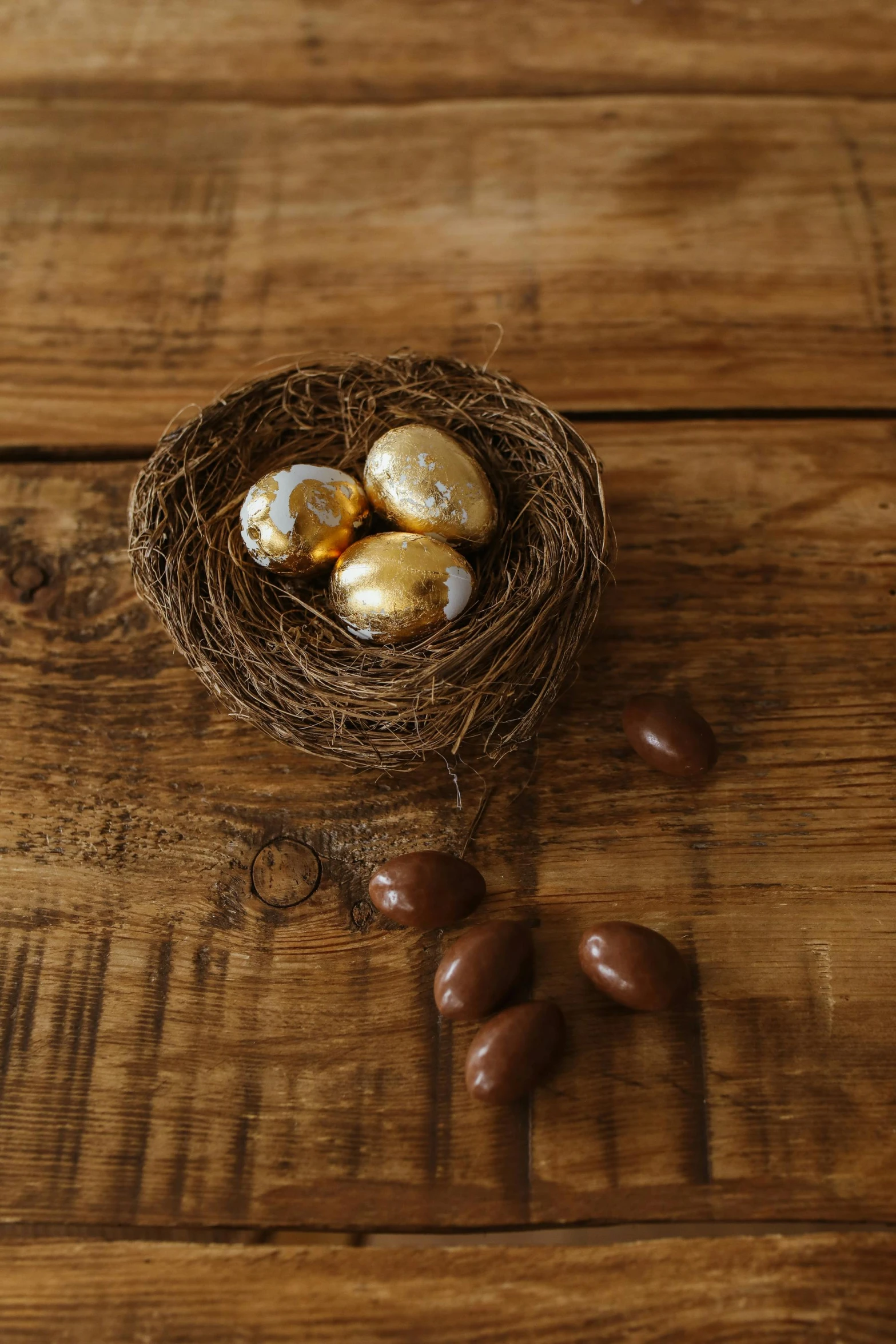 a nest filled with eggs sitting on top of a wooden table, fully chocolate, shiny gold, aussie, botanicals