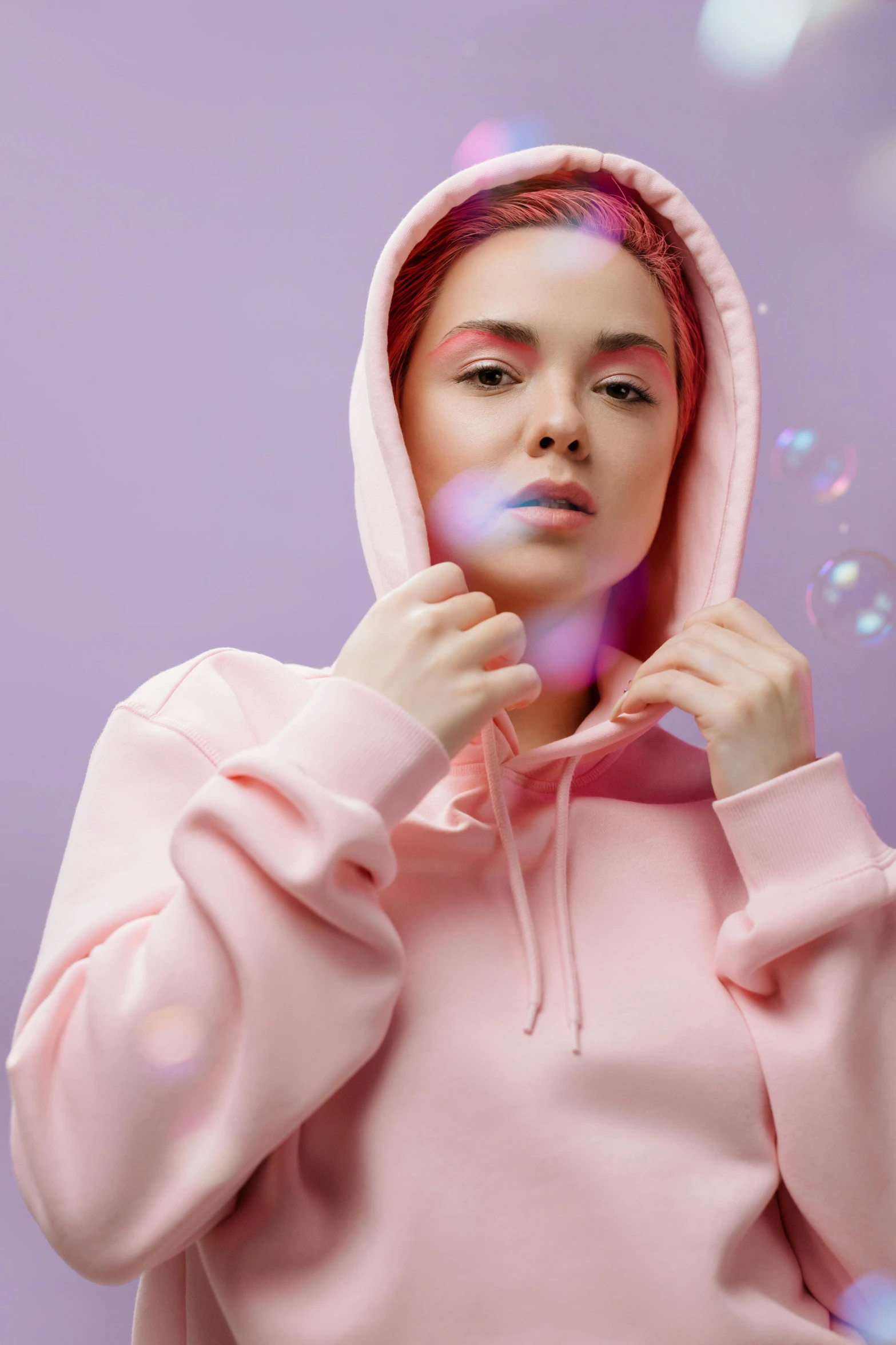a woman in a pink hoodie blowing bubbles, inspired by Elsa Bleda, trending on pexels, aestheticism, wearing a pastel pink hoodie, futuristic clothing, gif, looking serious