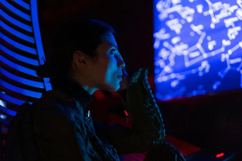 a woman sitting in front of a laptop computer, a hologram, inspired by Harry Clarke, interactive art, inside a space station, red and blue lighting, covered in circuitry, looking into the distance