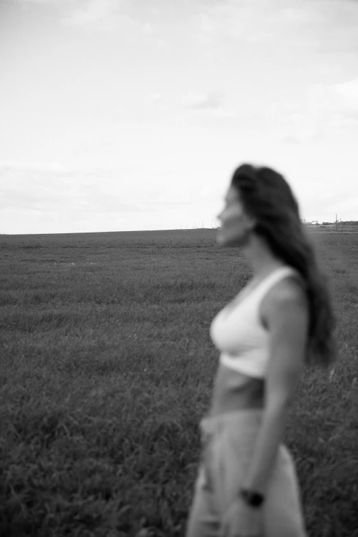 a black and white photo of a woman walking in a field, a black and white photo, happening, focus on torso, gazing off into the horizon, exposed midriff, movie filmstill