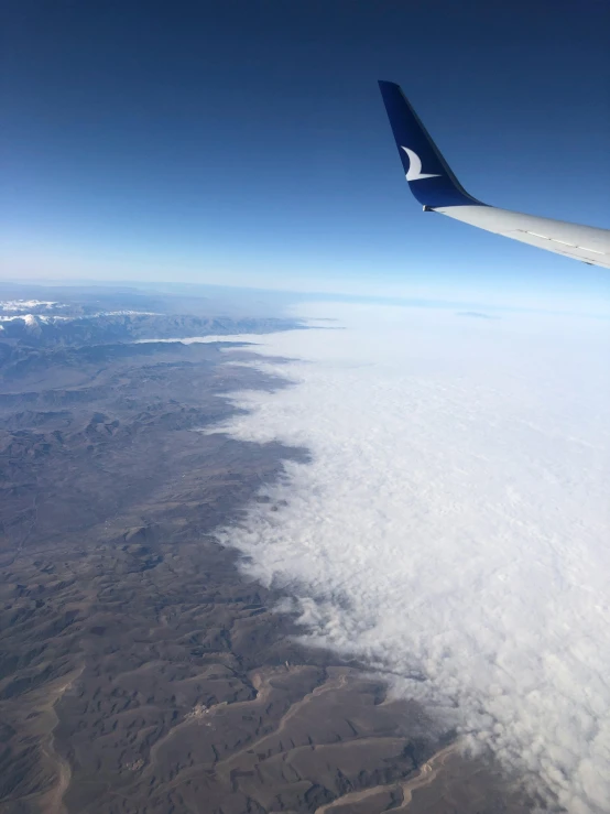 the wing of an airplane flying above the clouds, by Daren Bader, desert everywhere, snowy peaks, low quality photo, slightly foggy