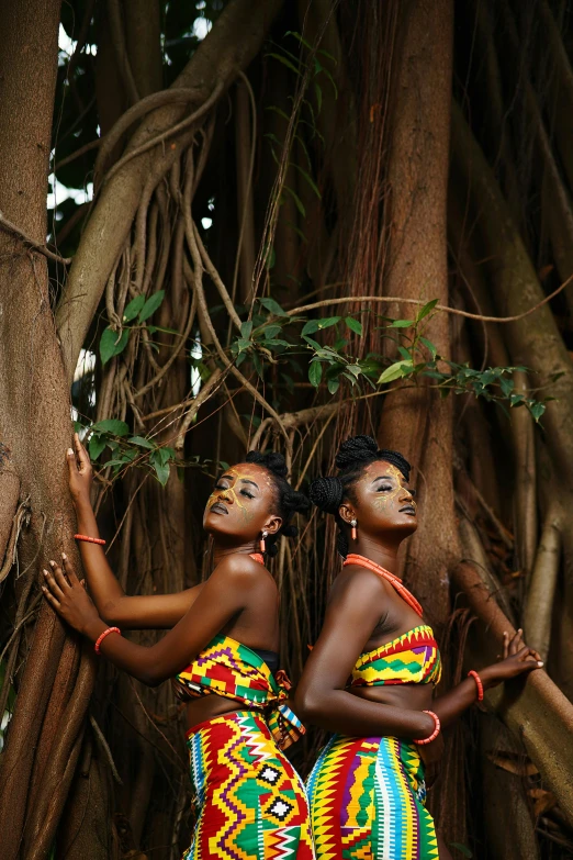 a couple of women standing next to a tree, by Ingrida Kadaka, pexels contest winner, afrofuturism, traditional makeup, majestic pose, twins, ( ( dark skin ) )