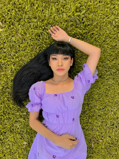 a woman laying on top of a lush green field, an album cover, inspired by Ren Hang, trending on pexels, purple outfit, gemma chan girl portrait, melanie martinez, high angle closeup portrait