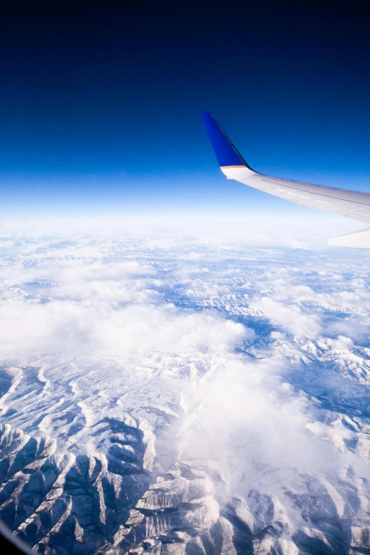 a view of snow capped mountains from an airplane window, by Daniel Taylor, trending on unsplash, fan favorite, blue, wing, looming over earth
